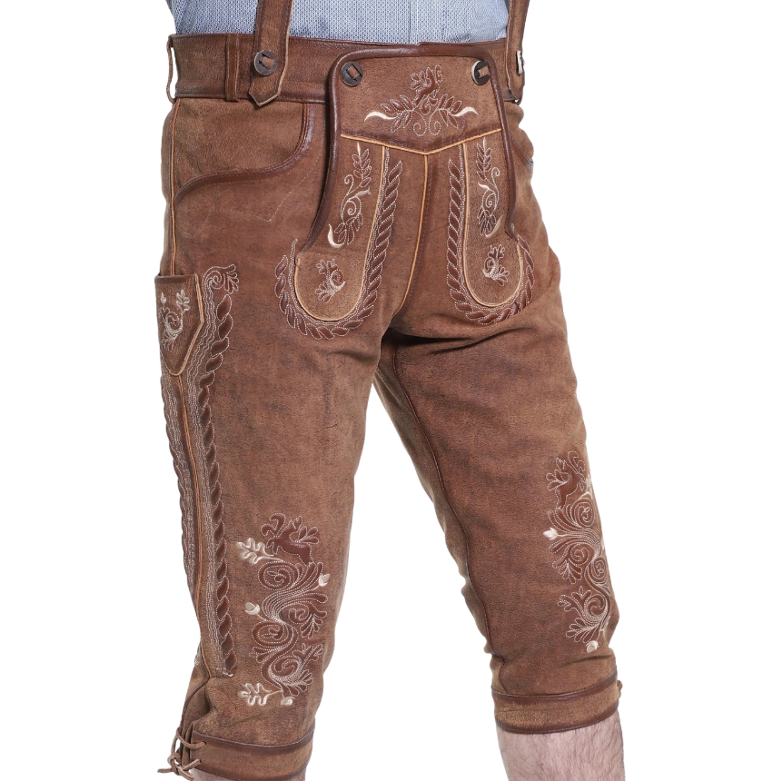 Angled front-side view of rustic oak leather bundhosen with ornate white embroidery, braided piping along the flap and thigh, and traditional drop-front closure.