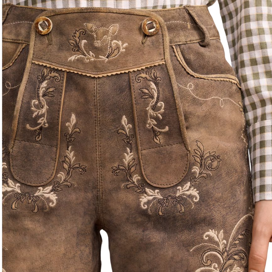 Close-up of floral embroidery on beige suede lederhosen shorts, showing decorative bib and pocket stitching.