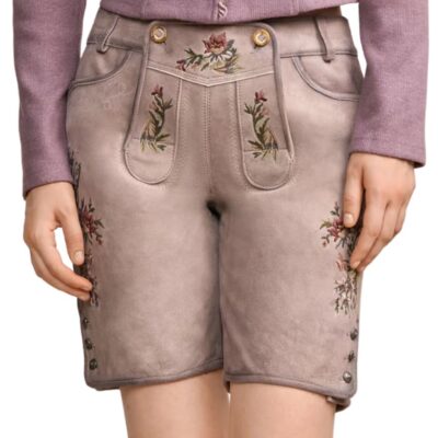A frontal view of traditional beige suede lederhosen shorts for women, featuring colorful floral embroidery, side buttons on the hem, and decorative front panel stitching, worn with a purple sweater Heritage Rose Suede